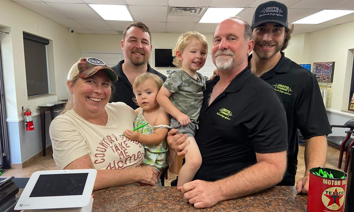 Team members and owners of Griffis Automotive Clinic pose for a photo in the shop office with 2 babies