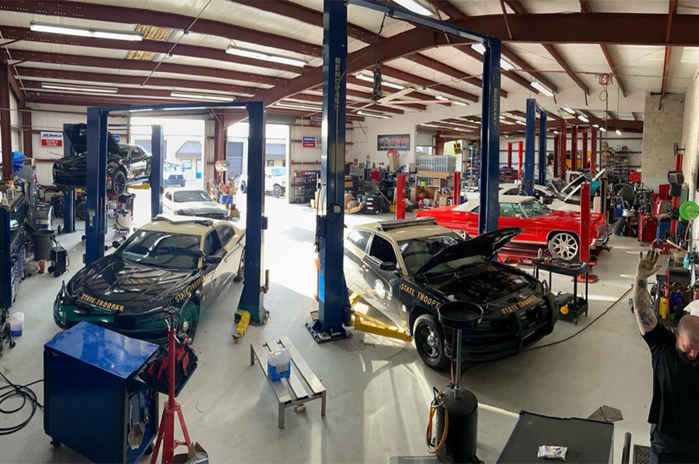 Looking for a reputable car mechanic in Groveland, FL? Image of Florida state trooper vehicles and other makes and model cars in the shop bay of Griffis Automotive Clinic in Groveland, FL. showcasing shop lifts, diagnostic tools, and machines for all auto repair needs with mechanic raising his hand.